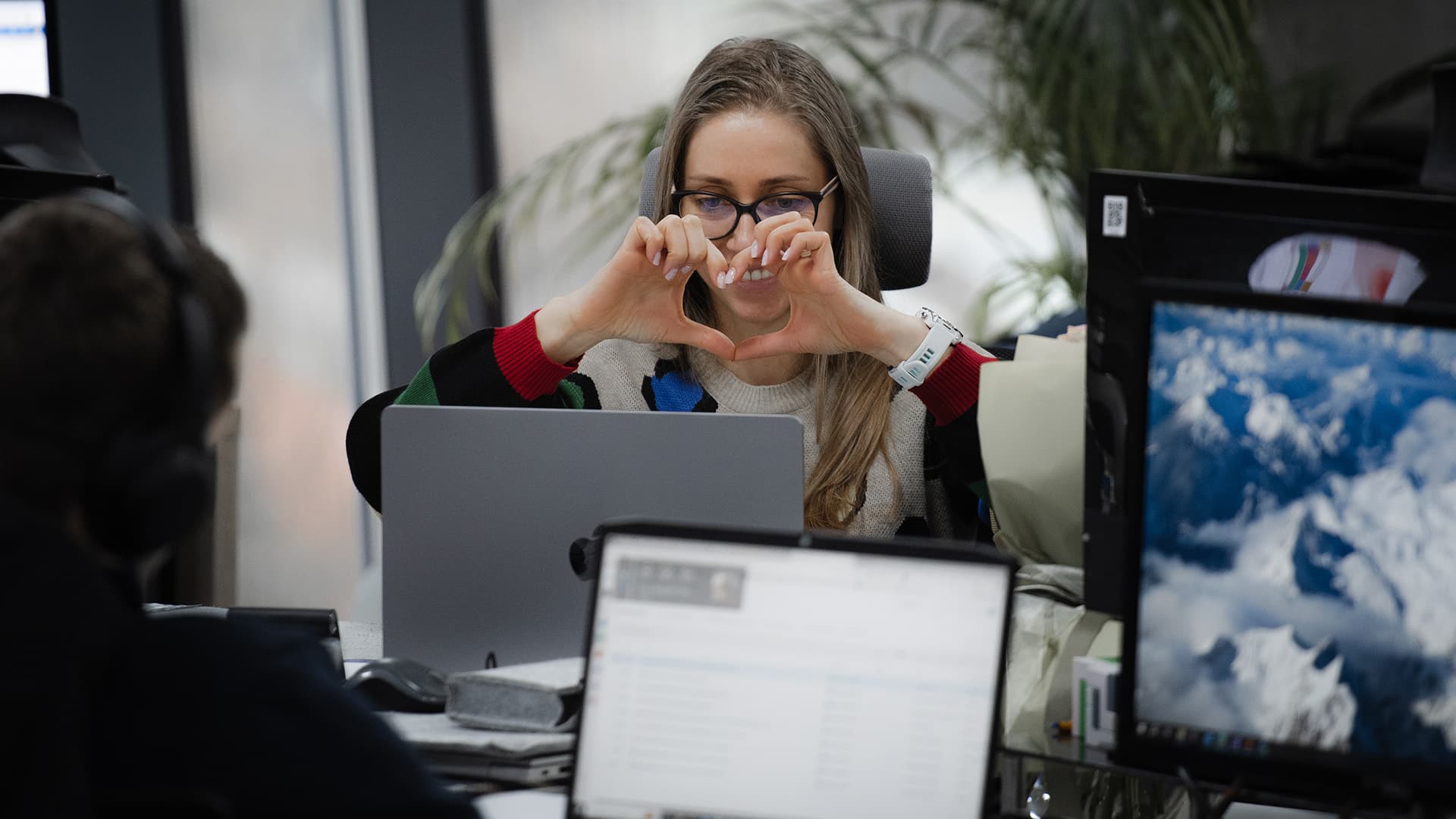 Kvindelig medarbejder viser hjerteform foran sin computer